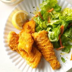 fried fish and salad on a plate with lemon wedges, lettuce and carrots