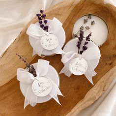 three small white dishes with lavenders in them on a wooden tray next to a candle