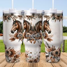 three travel mugs with horses on them sitting on a wooden table in front of a field