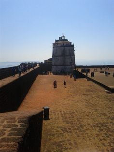 people are walking on the beach next to an old structure with a tower in the background