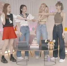 four young women standing around a table with a cake on it and one woman holding her hand out