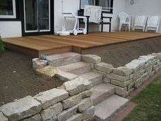 an outdoor patio with steps leading up to the front door and deck area, surrounded by rocks