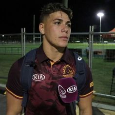 a young man wearing a maroon shirt and blue backpack holding a microphone in front of him