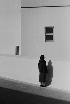 a woman standing in front of a building with her shadow on the wall behind her