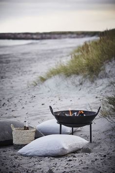 a fire pit sitting on top of a sandy beach next to the ocean and grass