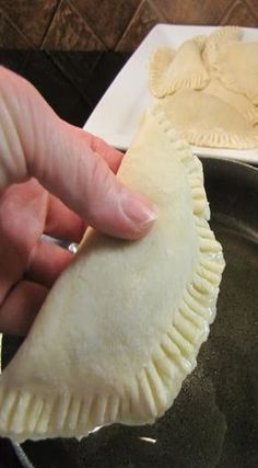 a hand holding a piece of food over a pan with another pie in the background