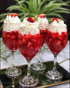 three glasses filled with strawberries and whipped cream sitting on top of a metal tray