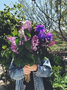 a woman holding a bouquet of purple flowers in her hands and wearing a jean jacket