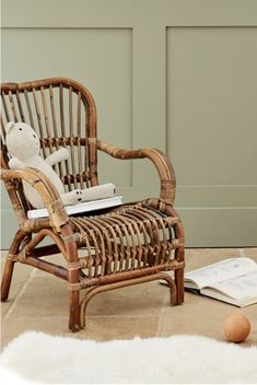 a wicker chair sitting on top of a white rug next to an open book