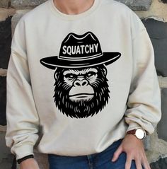 a man wearing a hat and sweatshirt with a monkey on it's back in front of a brick wall