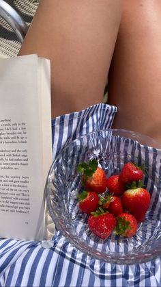 a glass bowl filled with strawberries next to an open book