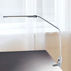 a desk lamp sitting on top of a wooden table in front of a window with white curtains