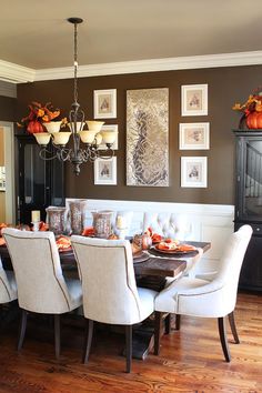 a dinning room table with white chairs and pictures on the wall above it,