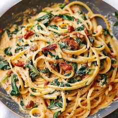 a plate full of pasta with spinach and bacon on top, ready to be eaten