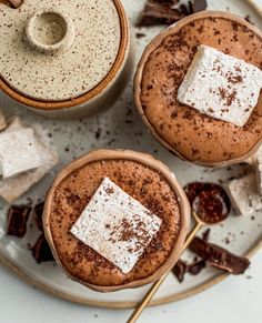 two mugs filled with hot chocolate and marshmallows on top of a plate