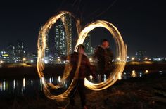 two people are standing near the water with fire spinning around them