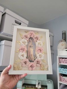 a person holding up a framed photo in front of some crafting supplies and sewing machines