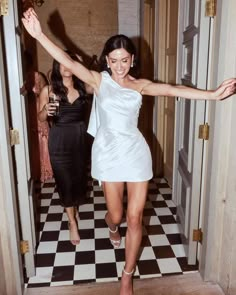 a woman in a short white dress is walking into a room with two other women