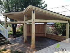 a wooden gazebo sitting on top of a brick patio next to a lush green forest