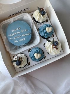 four cupcakes in a box with frosting and blue icing on them