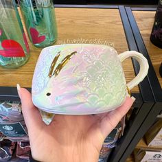 a hand holding a small ceramic fish shaped cup in front of a table with other items on it