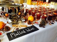 a table topped with lots of glasses filled with liquid next to a sign that says mulled wine