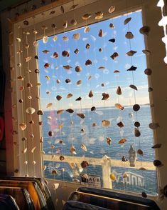 a window with sea shells hanging from it's side and the ocean in the background