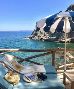 an umbrella and chair on a deck overlooking the water's edge, with a cell phone in front of it