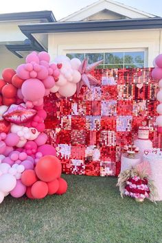 there are many balloons and decorations on the grass near a house that is decorated with red, pink and white colors