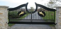 an iron gate with two gold horses on it's sides and a driveway in front