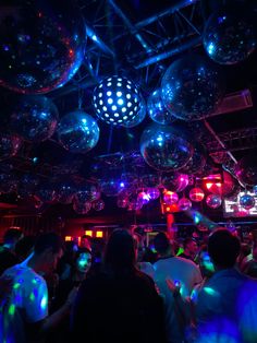 people are dancing at a party with disco balls hanging from the ceiling and lights on the ceiling