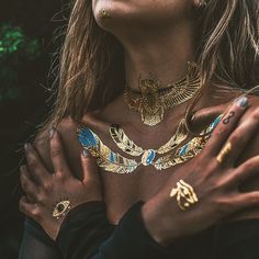 a close up of a person wearing gold jewelry and holding her hands on her chest