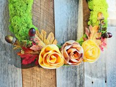 an arrangement of fake flowers and leaves on a wooden surface with moss in the background