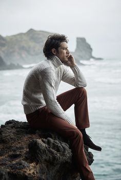 a man sitting on top of a rock next to the ocean