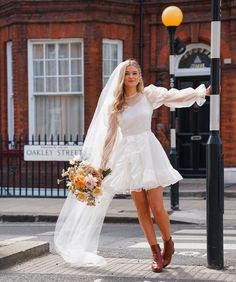 a woman in a short white dress is standing on the street corner with her veil over her head