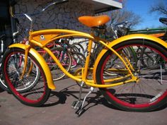 a yellow bicycle with red rims parked in front of a building next to other bicycles