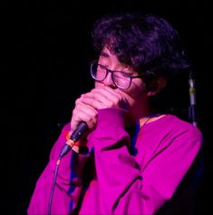 a young man with glasses on singing into a microphone in front of a black background