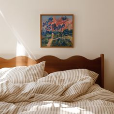 an unmade bed with a painting on the wall above it