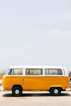 an old yellow and white van parked in a parking lot next to a tree filled field