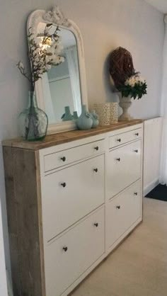 a white dresser sitting next to a mirror on top of a wooden floor