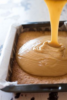 a person pouring peanut butter on top of a cake in a baking pan with the icing drizzled off