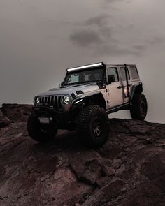 a jeep is parked on top of a rocky hill with dark clouds in the background