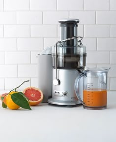 a silver juicer sitting on top of a counter next to oranges and other fruits