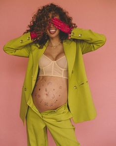 a pregnant woman in a green suit and red gloves covering her face with her hands