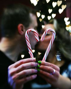 a man and woman kissing while holding candy canes