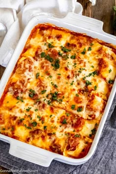 a casserole dish with cheese and parsley on top, sitting on a wooden table