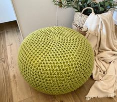 a large green knitted poufce sits on the floor next to a plant