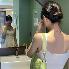 a woman standing in front of a bathroom mirror looking at her cell phone and holding a purse