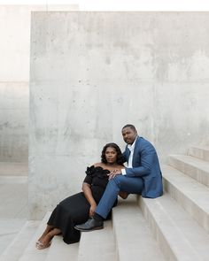 a man and woman sitting on the steps together in front of a cement wall, with their arms around each other