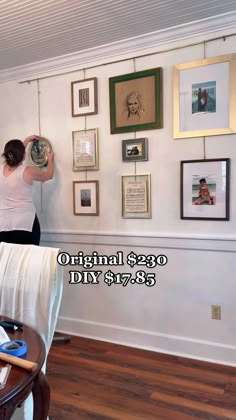 a woman is hanging pictures on the wall and holding a plate in front of her head